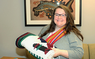 Megan Ellis, Indigenous Program Coordinator, holds a blanket and wears a red sash to show her Métis heritage.