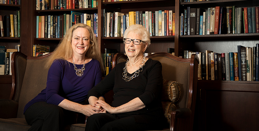 Melanie and Maureen sit in front of a wall of bookshelves