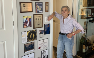 Dee Marcoux poses with her “wall of fame,” showcasing many instances of public recognition over a long career.