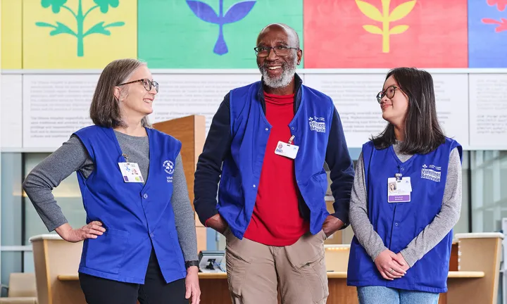 Three TOH volunteers wearing blue vests and ID badges stand together indoors.