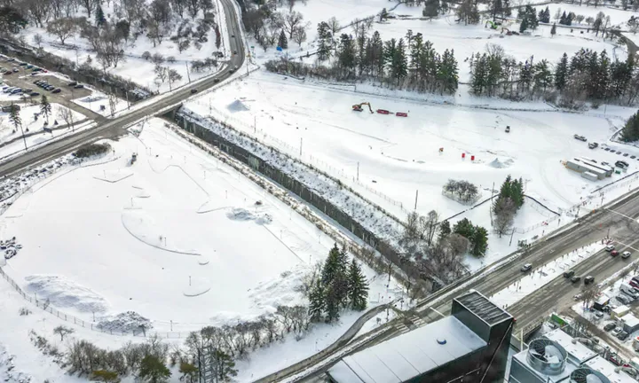 Vue aérienne, en hiver, du chantier enneigé où sera construit le stationnement à étages du nouveau campus de L’Hôpital d’Ottawa. Quelques engins de chantier, des remorques et un tracteur se trouvent sur le site. 