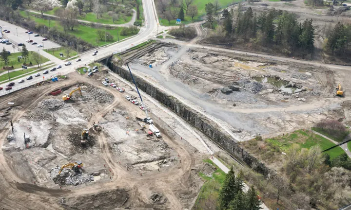 An aerial view in spring of the construction site where the parking garage for The Ottawa Hospital’s new campus will be built. Construction crews are excavating the ground with backhoes and other heavy equipment. 