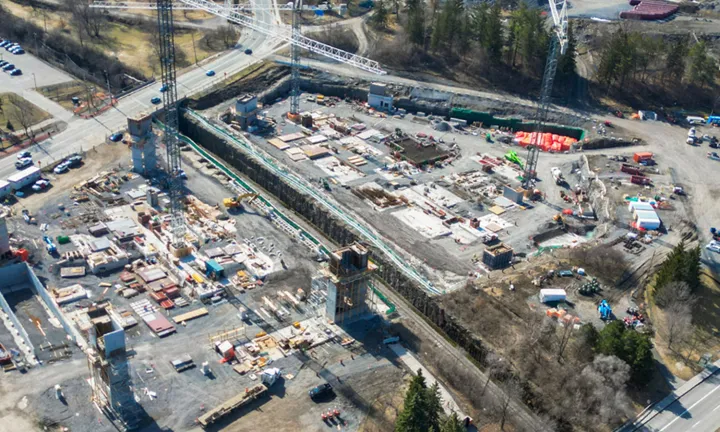 Vue aérienne, au début du printemps, du chantier de construction du stationnement à étages du nouveau campus de L’Hôpital d’Ottawa. Trois grandes grues à tour sont présentes sur le site. De grandes structures en béton telles que des cages d’escalier, des cages d’ascenseur et une rampe d’accès pour les véhicules sont partiellement construites et s’étendent verticalement à partir du niveau du sol. 