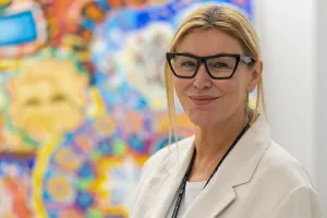Dr. Mary Marquardt stands in front of some colourful, therapeutic artwork created by clients in the OnTrack program.