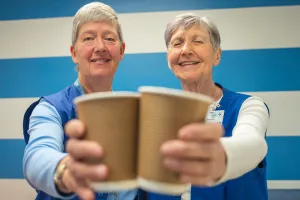 Volunteers Barb McDonald and Moninna Running holding are each holding up a cup of coffee