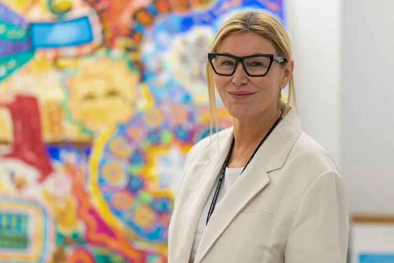 La Dre Mary Marquardt debout devant des créations d’art thérapeutique colorées faites par des clients du programme On avance. 