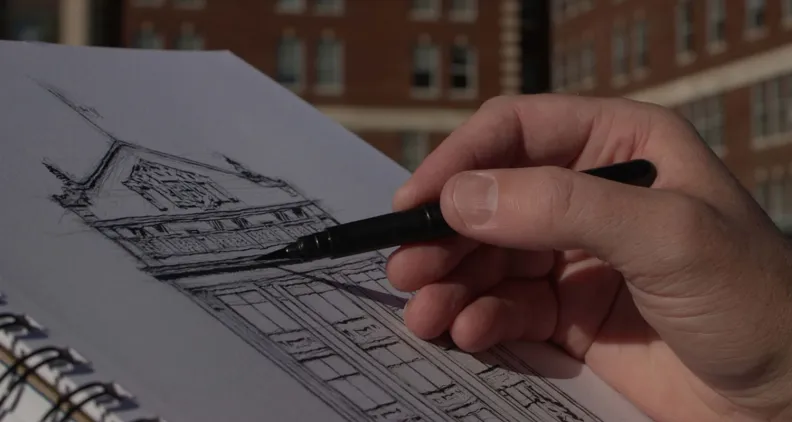 Close-up of an artist’s hand holding a sketch book, sketching the Civic Campus with a black market.