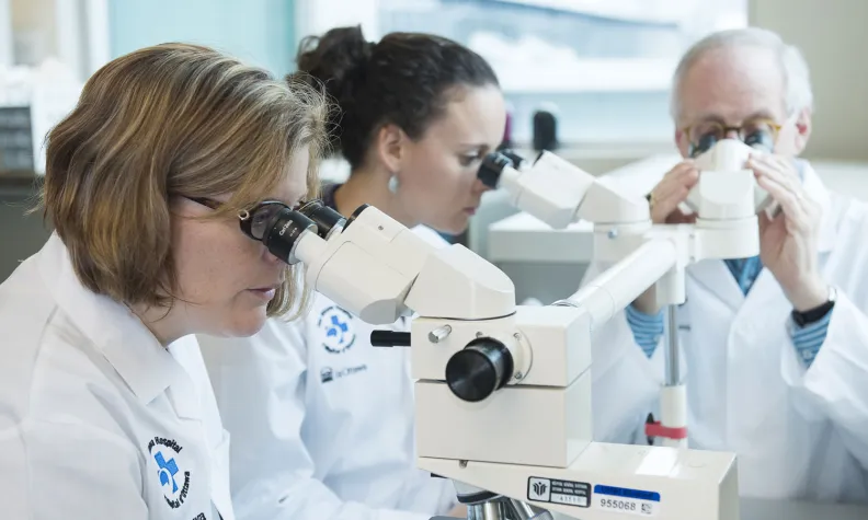 Trois scientifiques en sarrau blanc utilisent des microscopes dans un laboratoire.