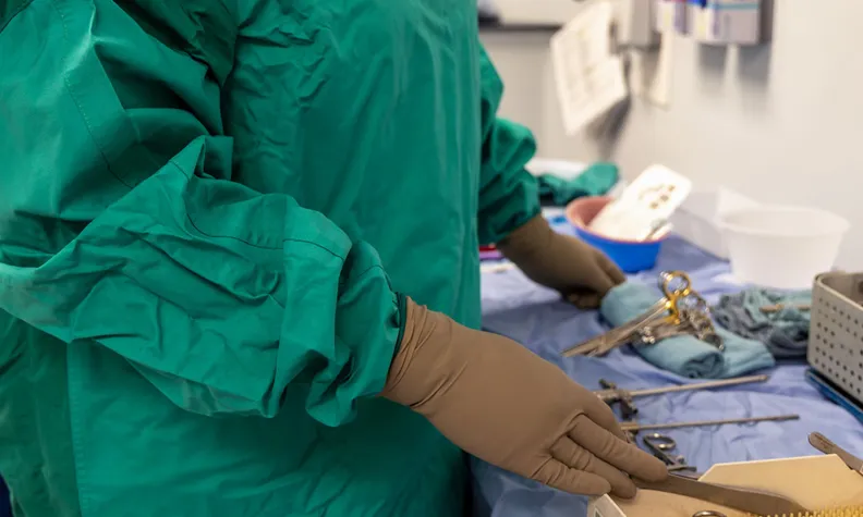 Close-up of task force member wearing green protective gowns and gloves while handling reusable medical instruments on a covered workspace.