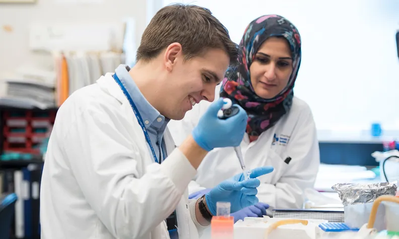 Two healthcare professionals in white coats are working together at a laboratory workbench, handling samples.