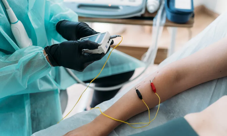 Au cours d’une intervention diagnostique, un professionnel de la santé portant des gants utilise un appareil électronique qui est relié par des fils et des électrodes à l’avant-bras d’un patient.