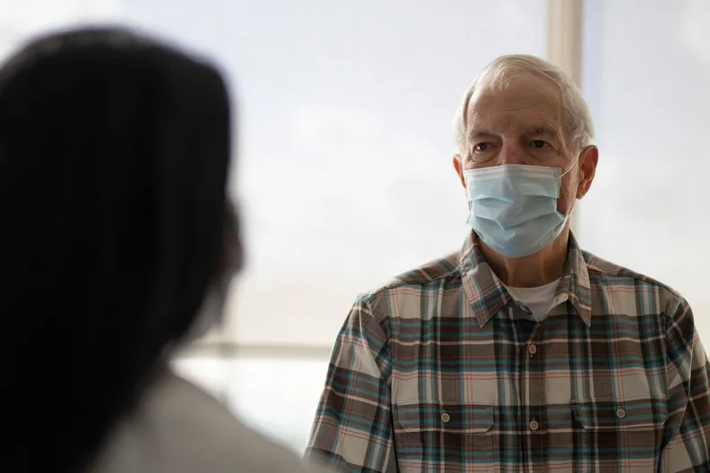 A healthcare provider speaks with an older adult wearing a mask.