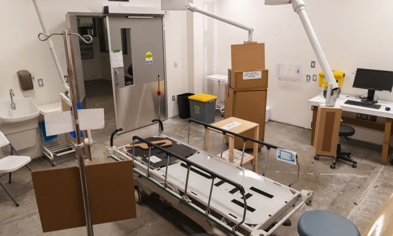 A high angle view inside a mock up of an endoscopy procedure room at a hospital. A stretcher is in the middle of the room, surrounded by artificial pieces of various hospital equipment.