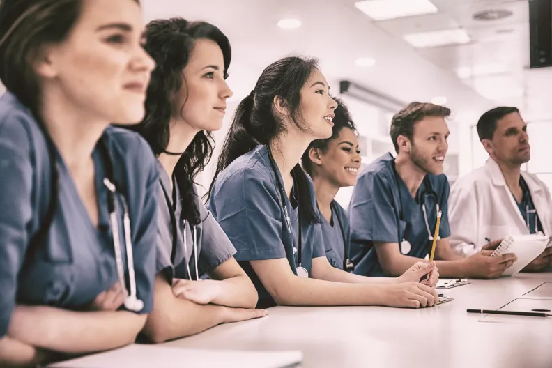 People in scrubs seated at a table during a medical training session.