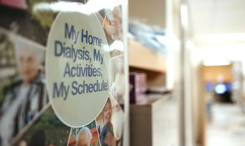 A round sign in a hallway reads, My Home, Dialysis, My Activities, My Schedule! The background is slightly blurred, showing shelves and a corridor, with indistinct images of people on the sign.