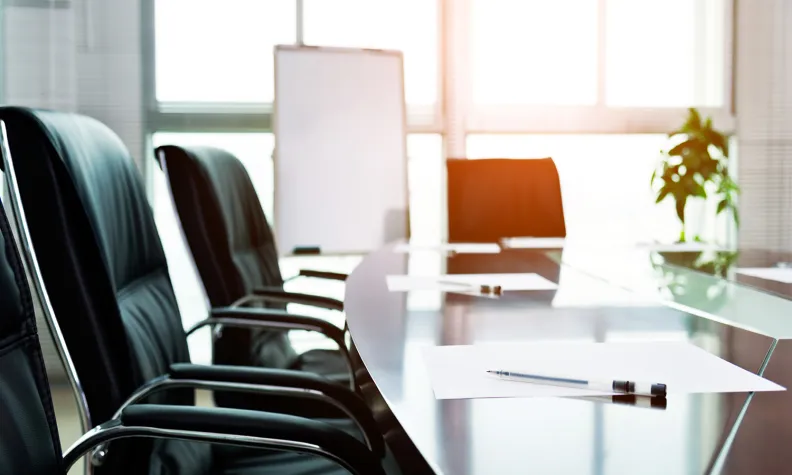 Empty conference room with chairs around a meeting table and a whiteboard in the background.