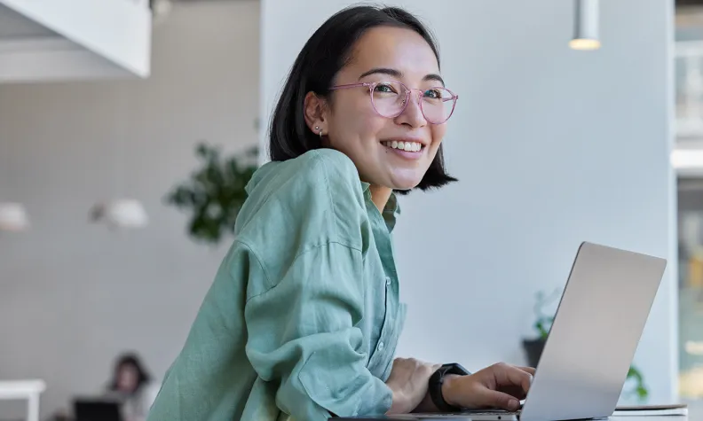 Person leaning on a desk while using a laptop in a bright, modern workspace.