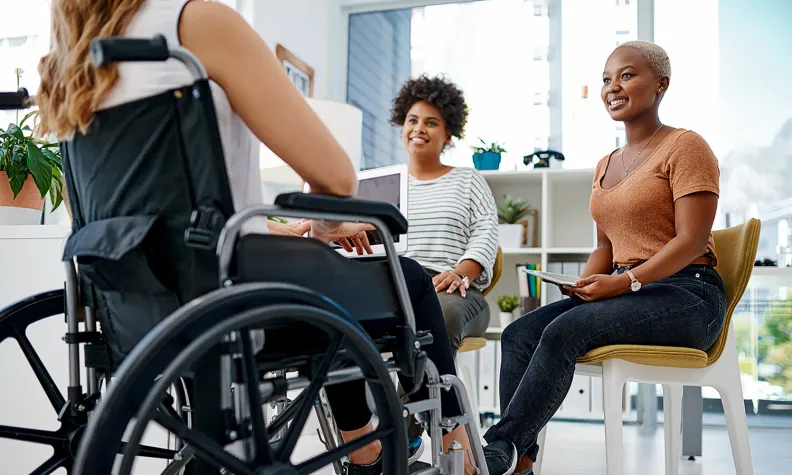 A person using a wheelchair sits in a meeting with two other people in an office setting.