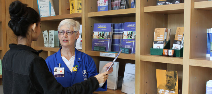 An Ottawa Hospital volunteer is showing someone a printed brochure in the Patient & Family Support and Resources Centres