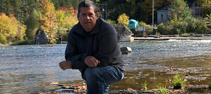 Stuart MacMillan kneeling in front of a river