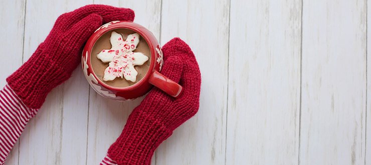 person wearing red mittens holding mug of hot chocolate
