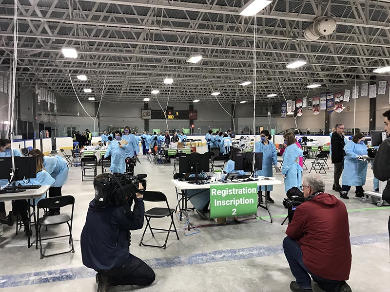 Des photographes prennent des photos du bureau d’inscription du Centre d’évaluation pour la COVID-19 de l’aréna Brewer.