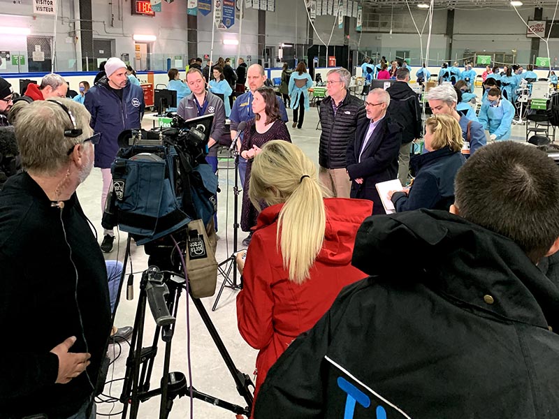 Dr. Vera Etches at a microphone in front of a media scrum inside of the Brewer Assessment Centre.