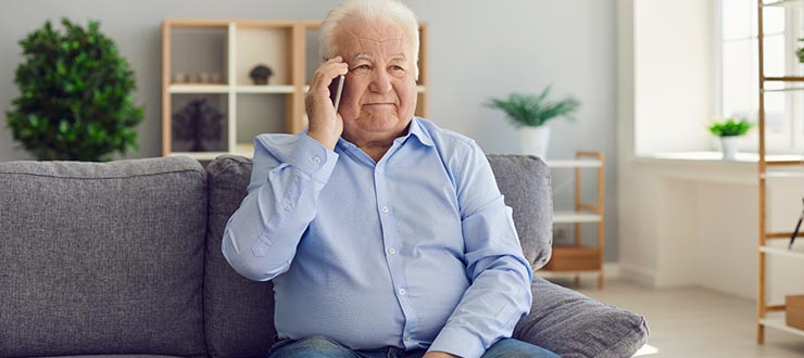 Older man sits on his couch and talks on the telephone