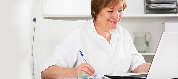 A woman sits in front of her laptop with a pen in her hand.