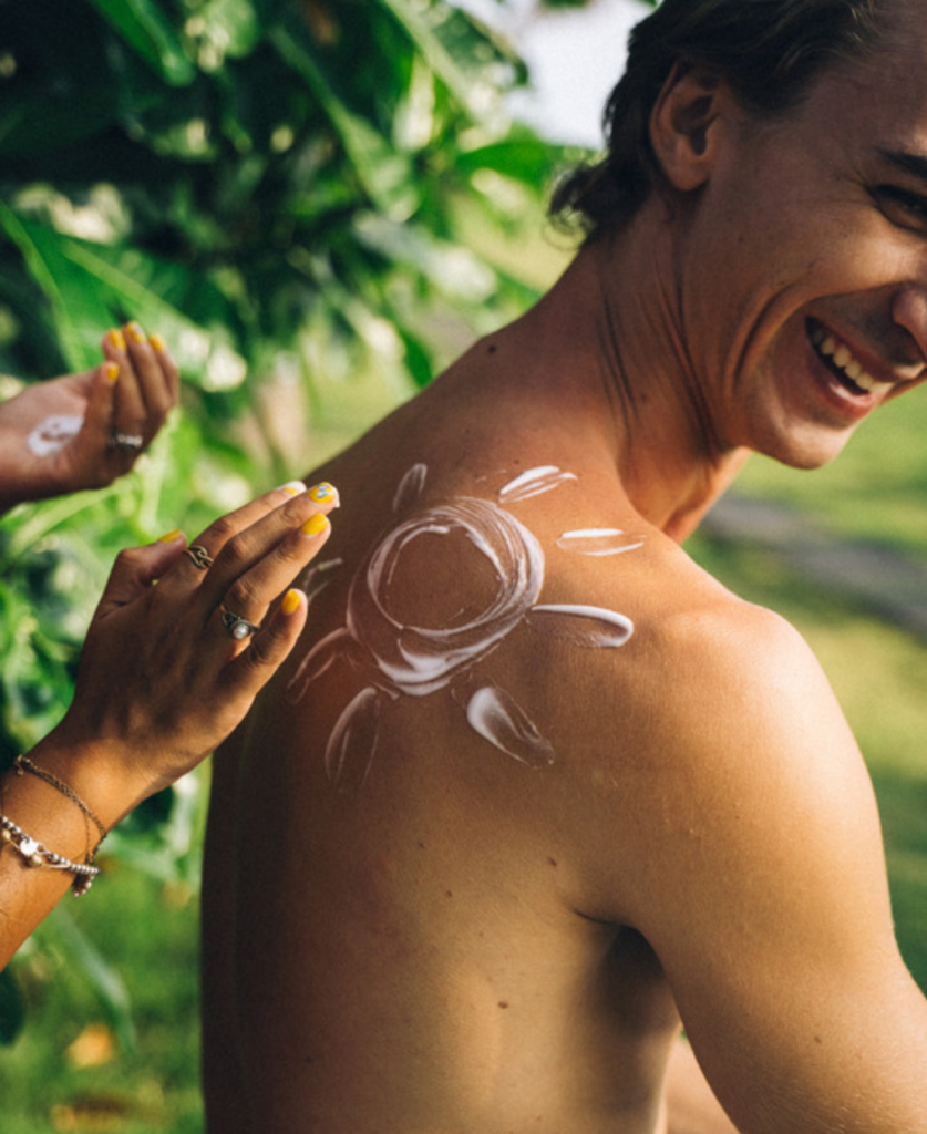 Person applying sunscreen in the shape of a sun on a man’s back