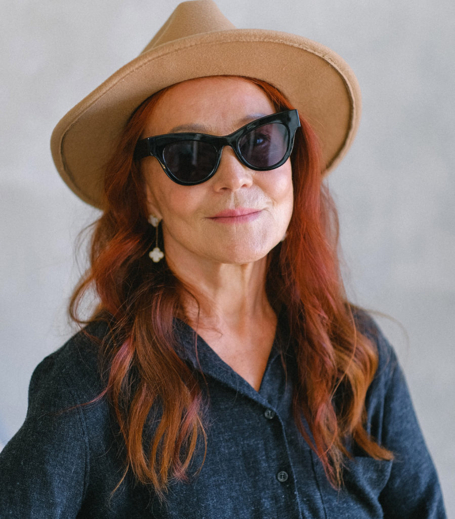 Older woman wearing a hat, sunglasses and a long-sleeved shirt