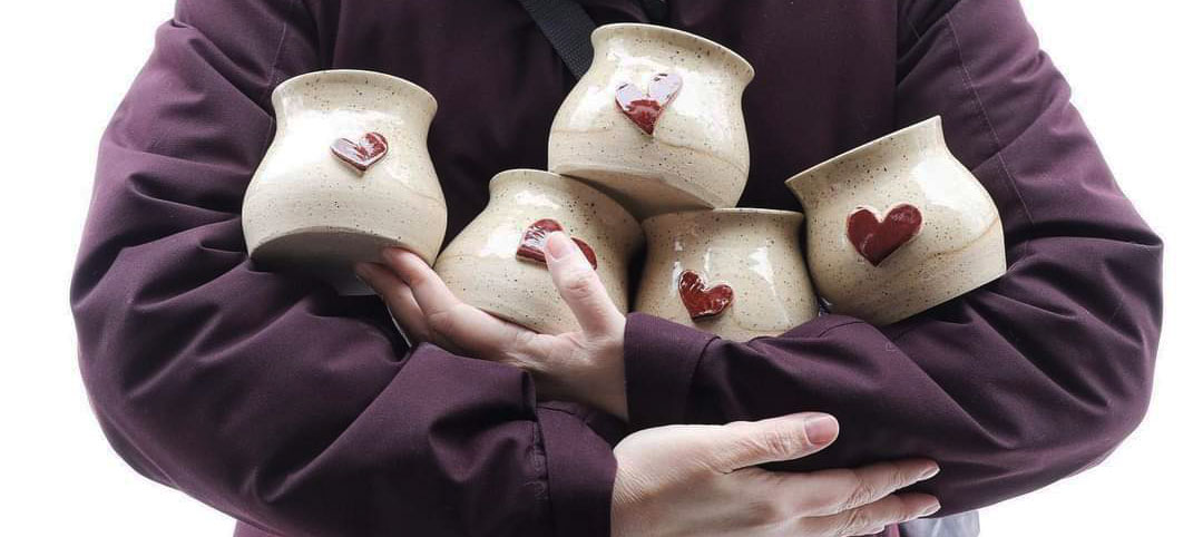 Woman in winter coat carrying five Heart Hug mugs