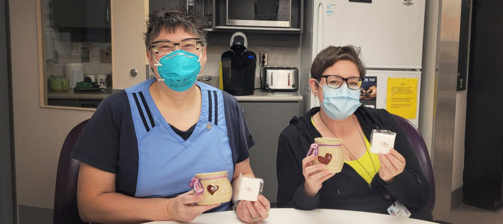 Two hospital staff sitting at a table holding their Heart Hug mugs.
