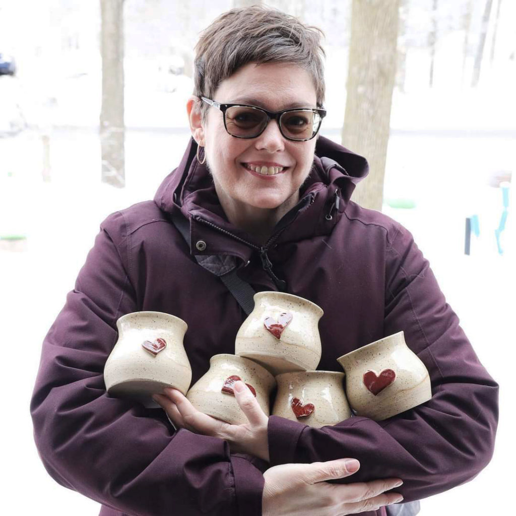 Une femme portant un manteau d’hiver tient dans ses bras cinq tasses ornées d’un cœur en relief.