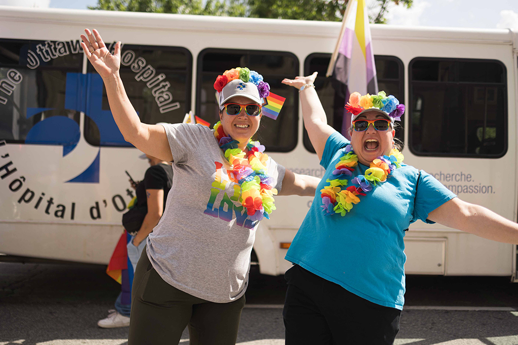 Melanie Finney (left) and Sarah Silverstein (right) wearing leis in front of The Ottawa Hospital’s shuttle bus.