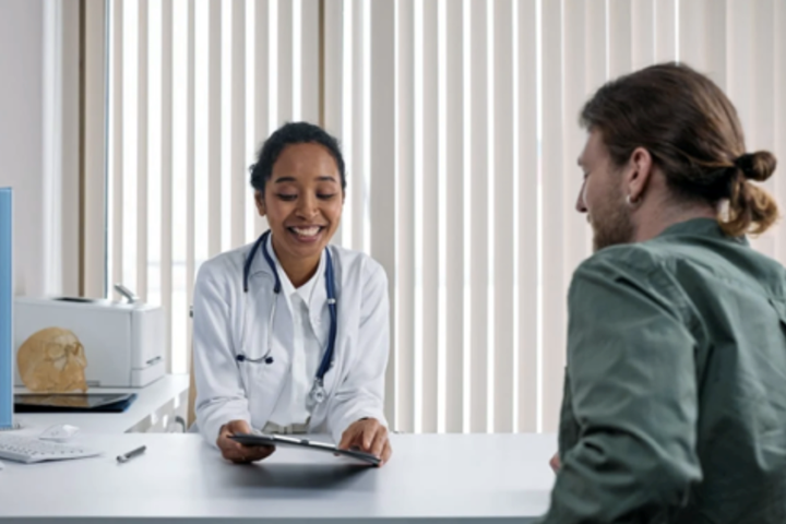 Professionnel de la santé souriant en regardant un dossier, assis à côté d’un patient