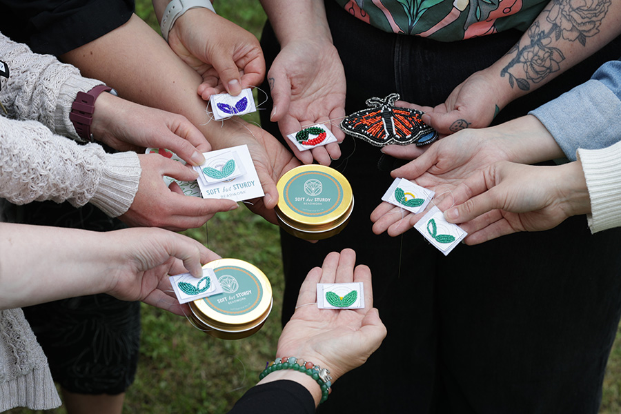 Groupe de personnes debout, formant un cercle et tenant leur création en perles, ainsi que les trousses à emporter préparées par Kaytlyn, l’animatrice de l’atelier.