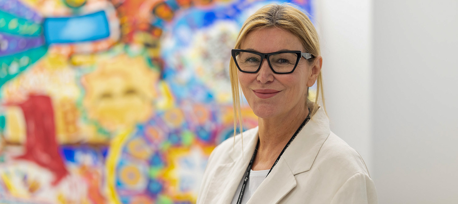 Dr. Mary Marquardt stands in front of some colourful, therapeutic artwork created by clients in the OnTrack program.