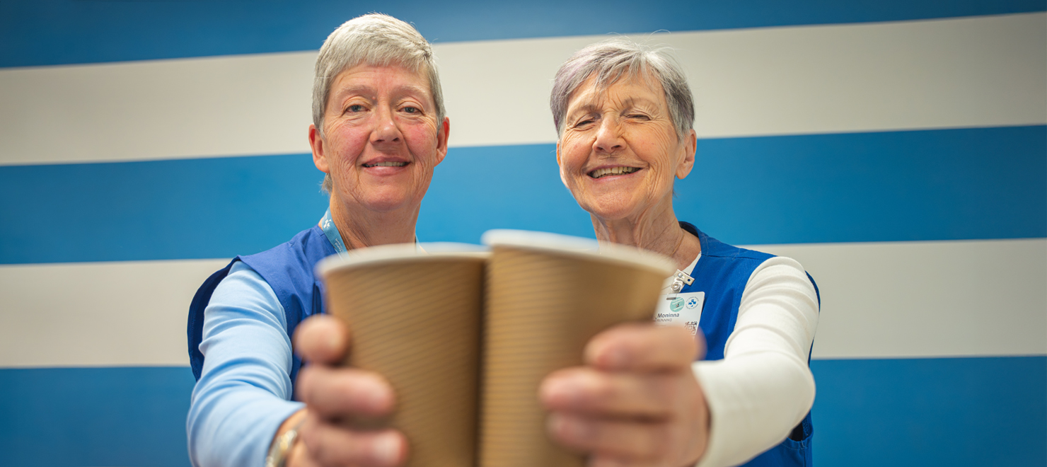 Volunteers Barb McDonald and Moninna Running holding are each holding up a cup of coffee