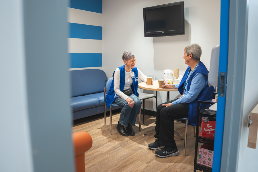Through a doorway, a view of volunteers Barb McDonald and Moninna Running sitting at a table and laughing